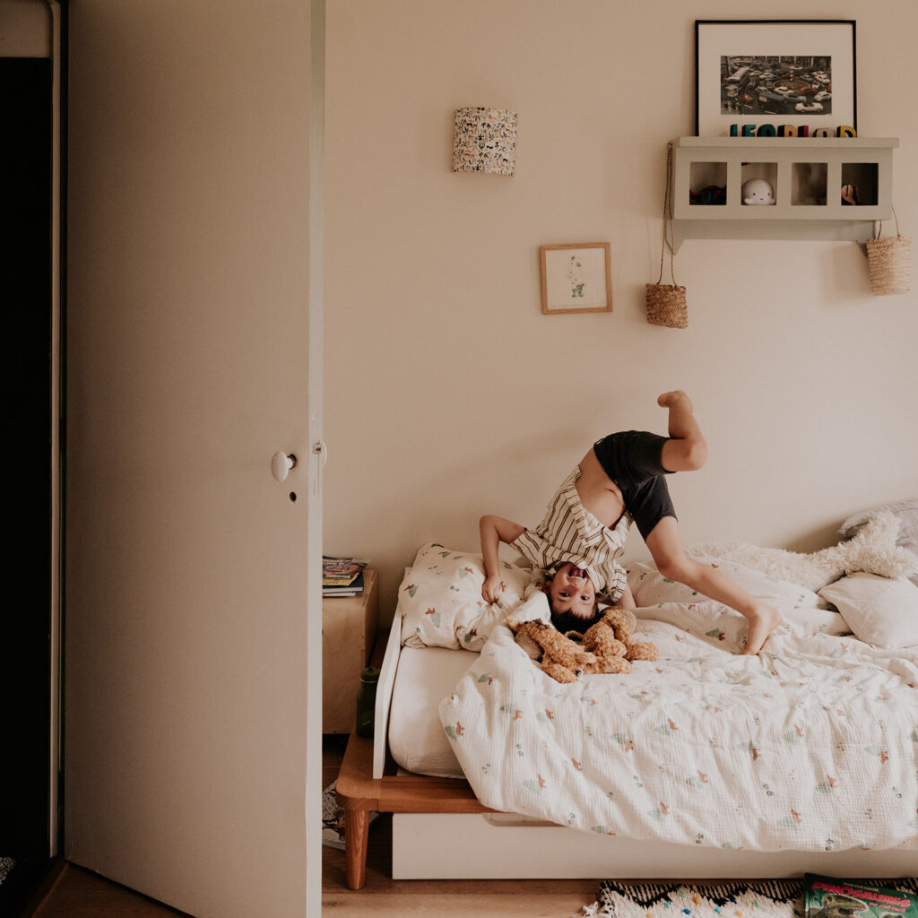 un petit garçon fait une roulade sur son lit, sous l'oeil de la photographe de famille.