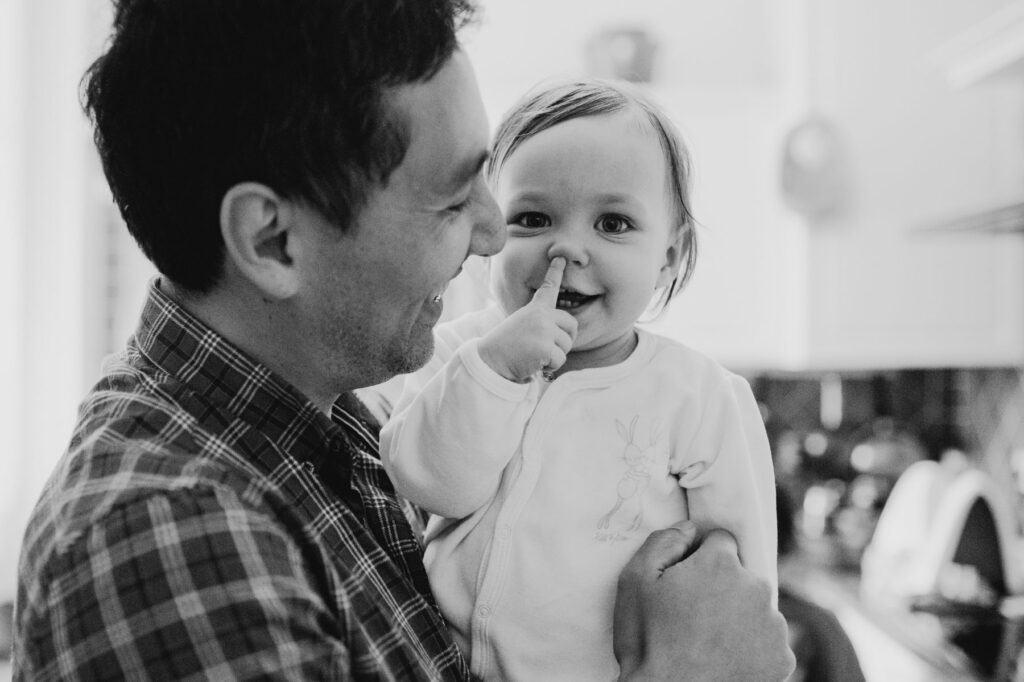 une petite fille dans les bras de son pere. elle met les doigts dans son nez