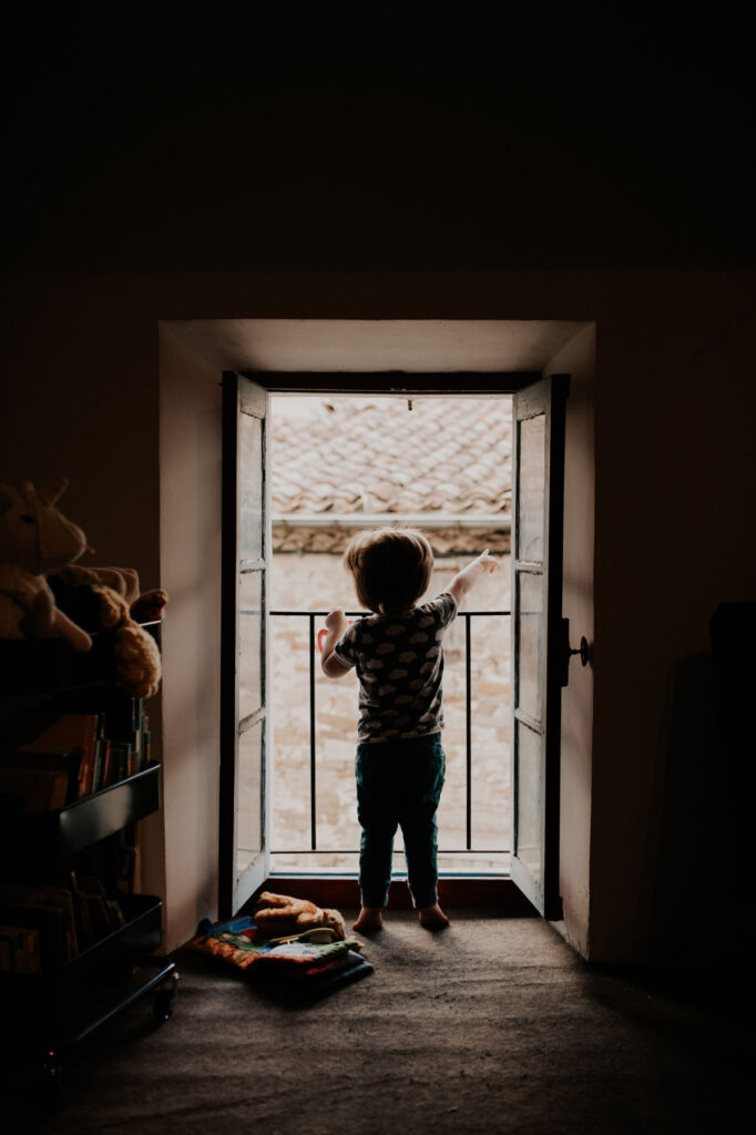 un enfant regarde par la fenêtre, de dos, en silhouette.