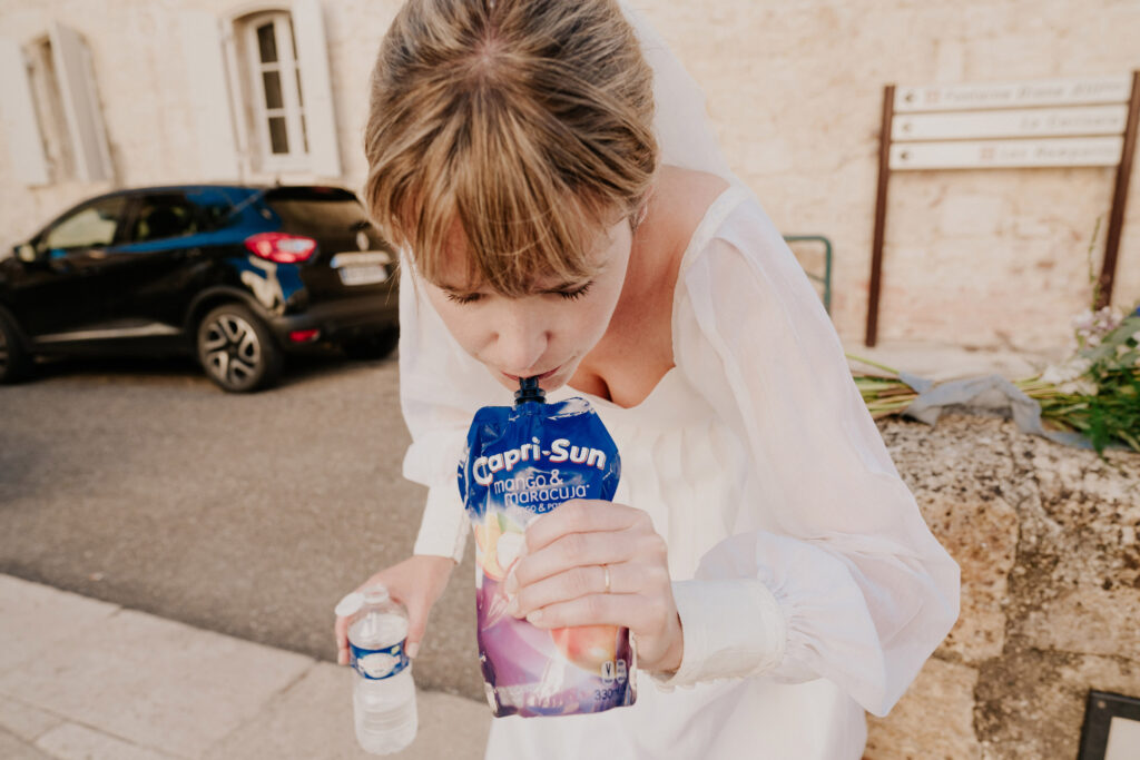 photo drôle d'une mariée qui boit un caprisun. Reportage photo de mariage authentique à Toulouse