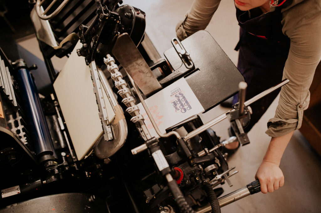 Artisan imprimeur en train de manipuler une presse typographique traditionnelle.