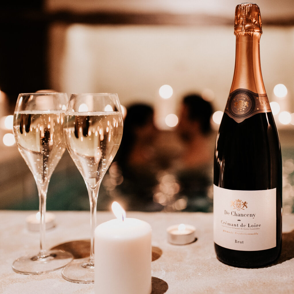 Bouteille de Chanceny et flûtes de champagne posées avec une bougie. devant des amoureux qui se baignent
