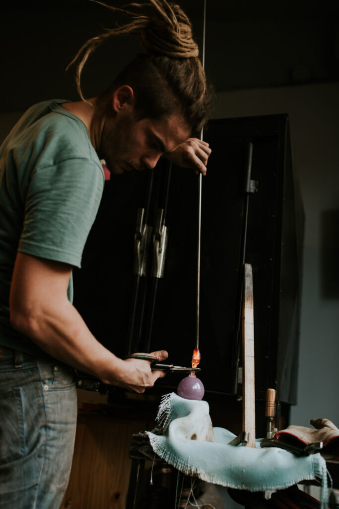 Souffleur de verre en train de façonner une pièce dans son atelier.